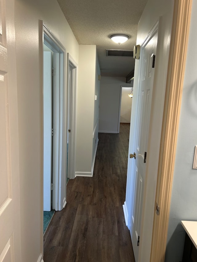 hall featuring dark wood-style floors, visible vents, a textured ceiling, and baseboards