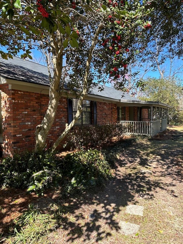 exterior space featuring covered porch, roof with shingles, and brick siding