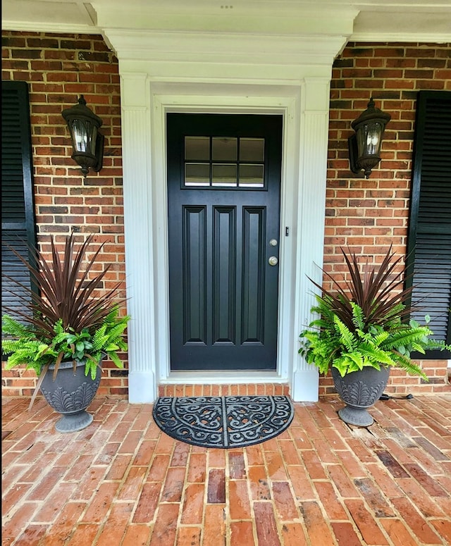 view of exterior entry featuring a porch and brick siding