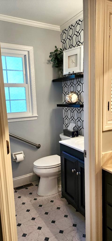 bathroom featuring toilet, vanity, ornamental molding, visible vents, and baseboards