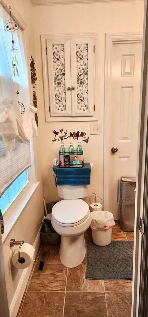 bathroom with baseboards, ornamental molding, visible vents, and toilet