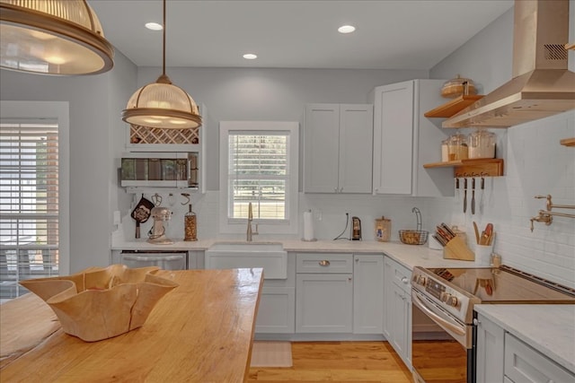 kitchen featuring pendant lighting, wall chimney range hood, appliances with stainless steel finishes, white cabinets, and light wood-type flooring