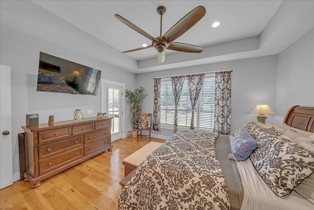 bedroom featuring access to outside, light hardwood / wood-style flooring, ceiling fan, and a tray ceiling