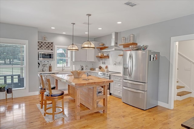 kitchen with pendant lighting, appliances with stainless steel finishes, tasteful backsplash, white cabinets, and wall chimney exhaust hood