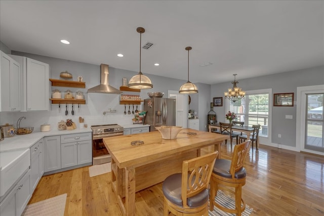 kitchen featuring white cabinets, hanging light fixtures, stainless steel appliances, wall chimney range hood, and light wood-type flooring