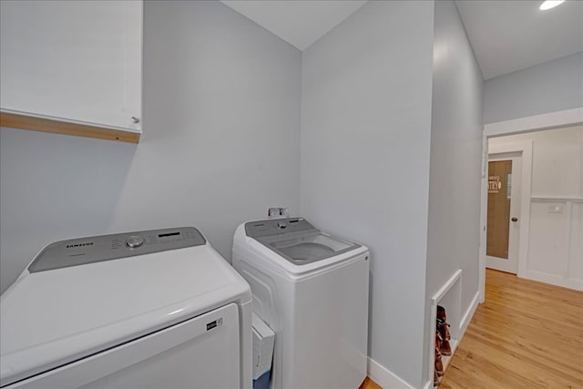 laundry area with separate washer and dryer, light hardwood / wood-style floors, and cabinets