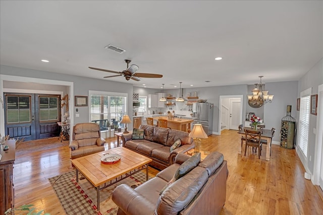 living room featuring ceiling fan with notable chandelier and light hardwood / wood-style floors