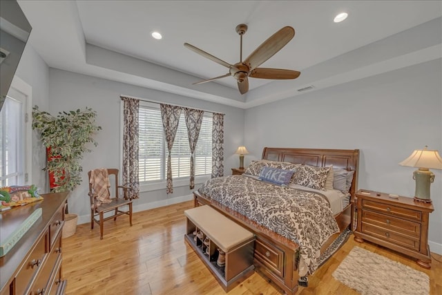 bedroom with ceiling fan, light hardwood / wood-style floors, and a tray ceiling