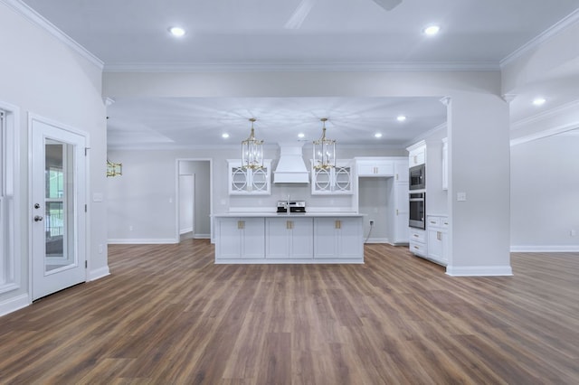 kitchen with premium range hood, appliances with stainless steel finishes, white cabinetry, a kitchen island with sink, and a notable chandelier