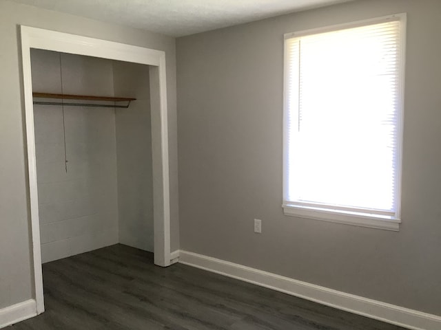 unfurnished bedroom featuring dark wood-style floors, baseboards, and a closet