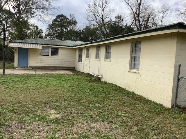 view of side of property featuring concrete block siding, metal roof, and a yard