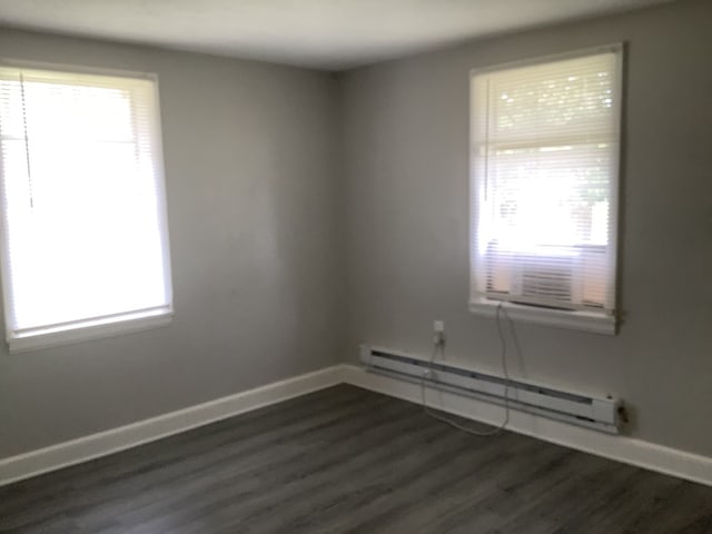 empty room with a baseboard heating unit, dark wood finished floors, and baseboards