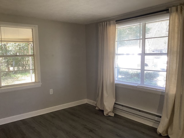 empty room with dark wood-style floors, a baseboard heating unit, and baseboards