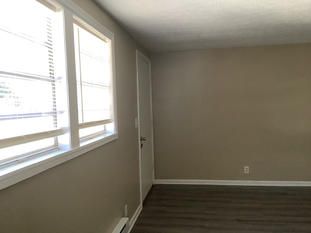 unfurnished room with a textured ceiling, dark wood-style floors, and baseboards