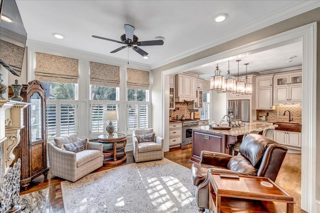 living room featuring sink, hardwood / wood-style floors, ceiling fan with notable chandelier, and ornamental molding