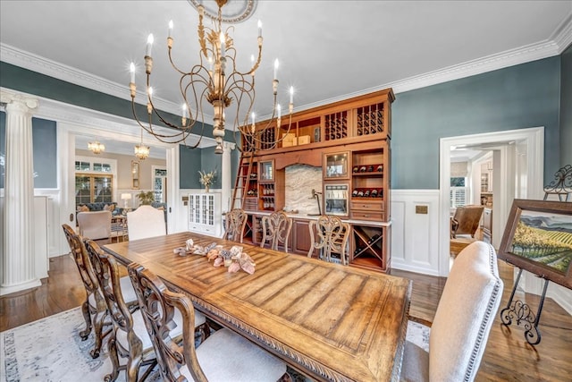 dining room with decorative columns, crown molding, dark wood-type flooring, and an inviting chandelier