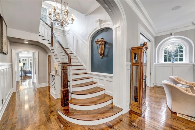 stairway featuring wood-type flooring, crown molding, and a notable chandelier