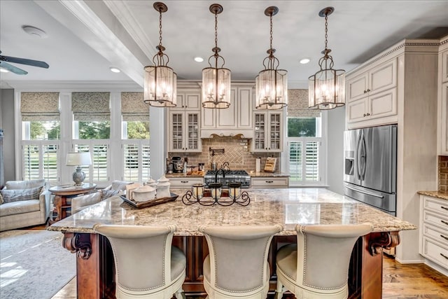 kitchen featuring stainless steel refrigerator with ice dispenser, pendant lighting, a breakfast bar, backsplash, and a large island with sink