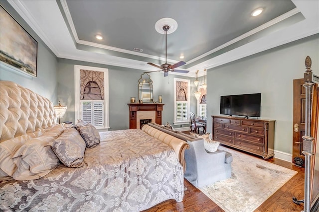 bedroom with crown molding, ceiling fan, a raised ceiling, multiple windows, and hardwood / wood-style floors