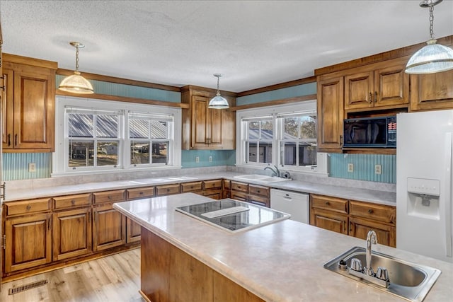 kitchen with black appliances, hanging light fixtures, light hardwood / wood-style floors, and sink