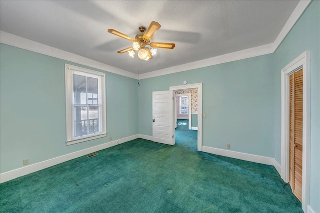 unfurnished bedroom with a textured ceiling, a closet, dark colored carpet, ornamental molding, and ceiling fan