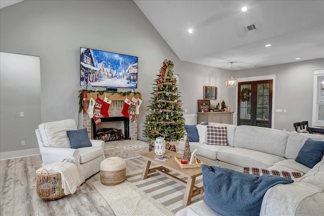 living room featuring light wood-type flooring, french doors, a brick fireplace, and lofted ceiling