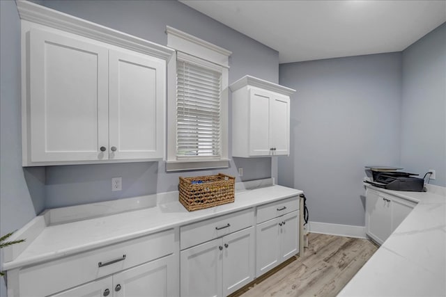 kitchen with light stone counters, white cabinetry, and light hardwood / wood-style flooring