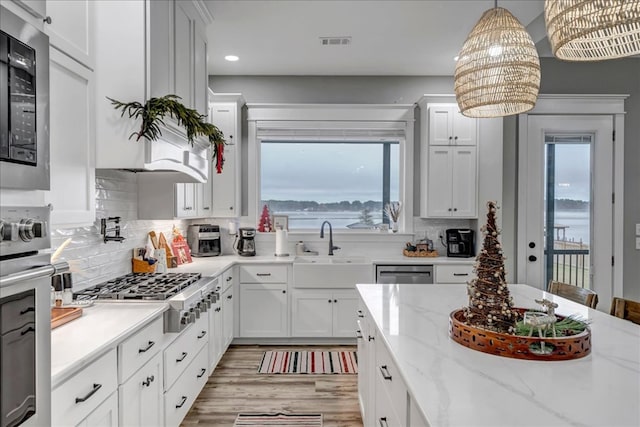 kitchen with hanging light fixtures, appliances with stainless steel finishes, white cabinets, a healthy amount of sunlight, and decorative backsplash