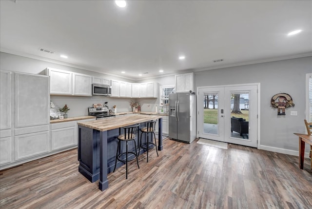 kitchen featuring appliances with stainless steel finishes, hardwood / wood-style flooring, white cabinetry, a kitchen breakfast bar, and ornamental molding