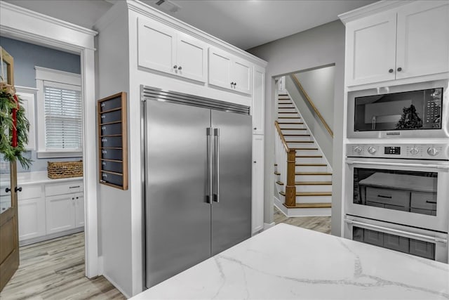 kitchen featuring light stone countertops, white cabinetry, built in appliances, and light wood-type flooring