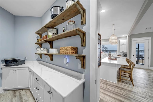 kitchen featuring hanging light fixtures, white cabinets, light hardwood / wood-style flooring, kitchen peninsula, and light stone counters