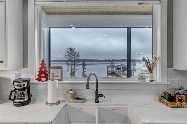 room details featuring light stone countertops, sink, a water view, and tasteful backsplash