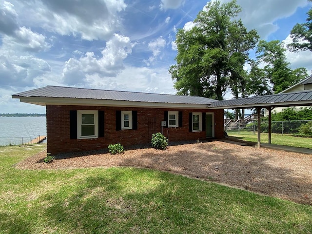 ranch-style home featuring a water view, fence, metal roof, a front lawn, and brick siding