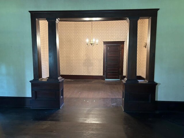 hall with ornate columns, dark wood-type flooring, and an inviting chandelier