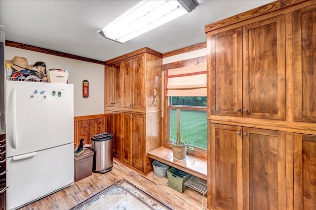 kitchen with a textured ceiling, ornamental molding, light hardwood / wood-style flooring, wood walls, and white refrigerator