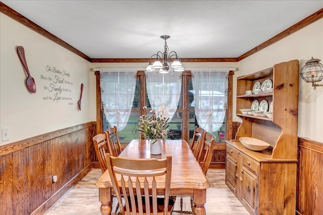 dining space featuring a notable chandelier, light wood-type flooring, crown molding, and wooden walls