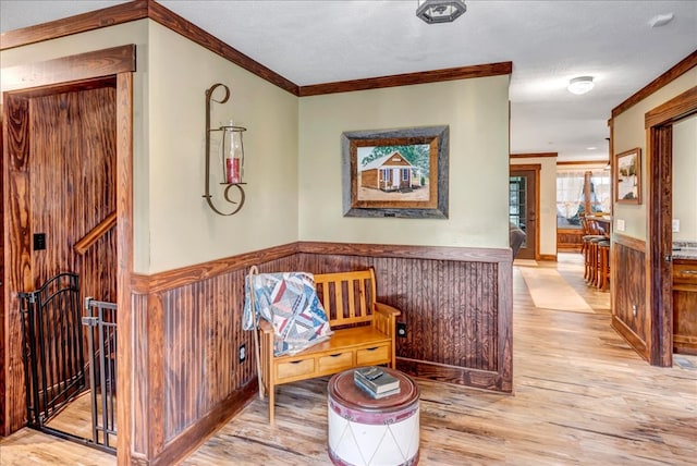 living area with crown molding, a textured ceiling, light hardwood / wood-style flooring, and wooden walls