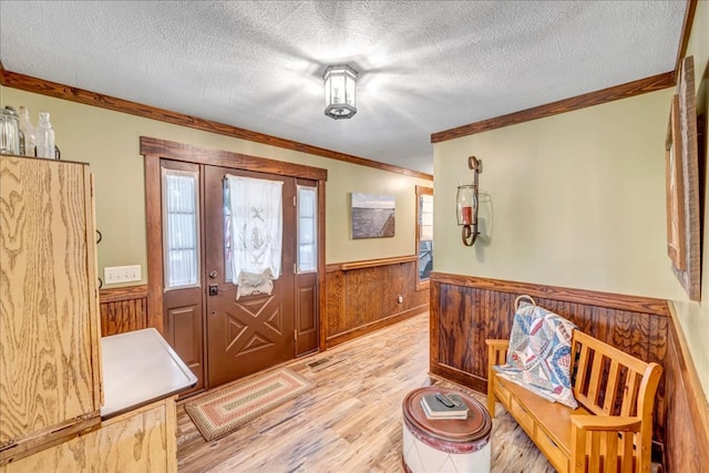 foyer with crown molding, light hardwood / wood-style floors, a textured ceiling, and wooden walls