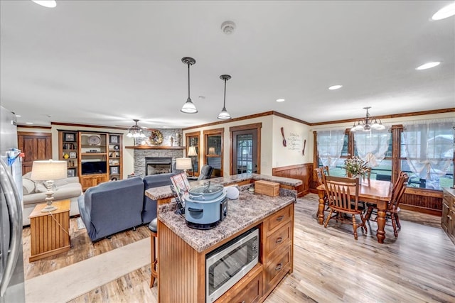 kitchen with stainless steel microwave, decorative light fixtures, a fireplace, a kitchen island, and wood walls