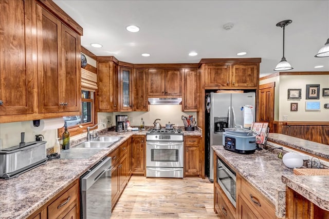 kitchen with light stone countertops, appliances with stainless steel finishes, decorative light fixtures, light hardwood / wood-style floors, and sink