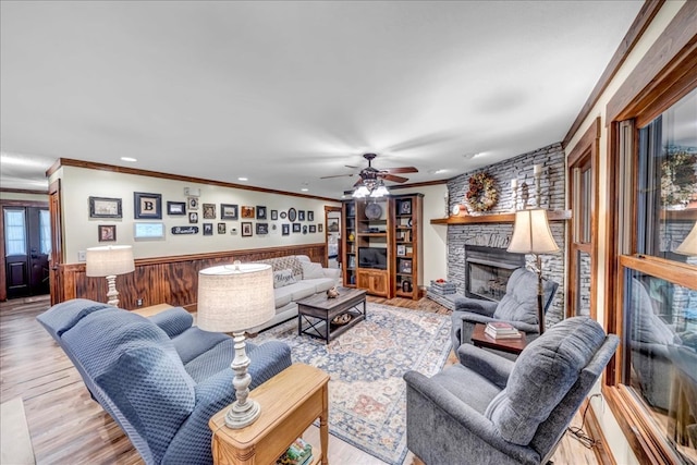 living room featuring crown molding, ceiling fan, a fireplace, wood walls, and light hardwood / wood-style floors