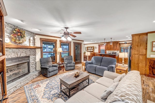 living room with a fireplace, light wood-type flooring, ceiling fan, and ornamental molding