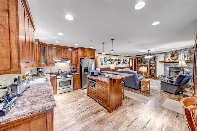 kitchen featuring pendant lighting, appliances with stainless steel finishes, sink, light stone counters, and a kitchen island