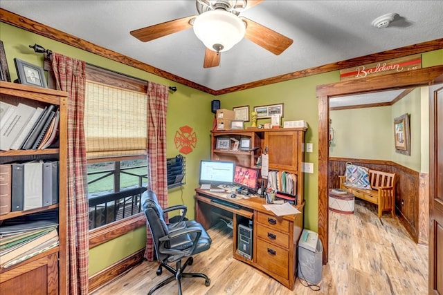 home office featuring a textured ceiling, wooden walls, ornamental molding, ceiling fan, and light hardwood / wood-style flooring