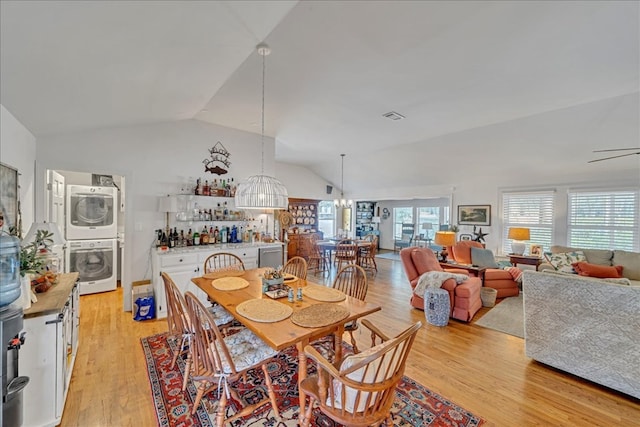 dining area featuring light wood-type flooring, stacked washer and clothes dryer, visible vents, and lofted ceiling