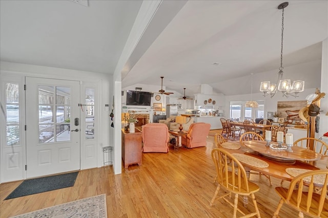 foyer featuring lofted ceiling, a fireplace, light wood finished floors, and ceiling fan with notable chandelier