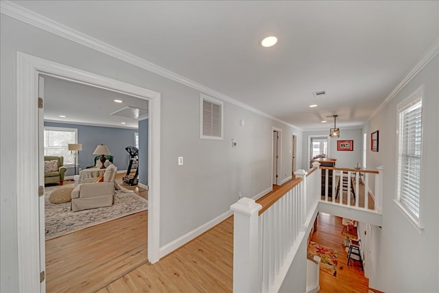 hallway with visible vents, ornamental molding, an upstairs landing, and light wood-style floors