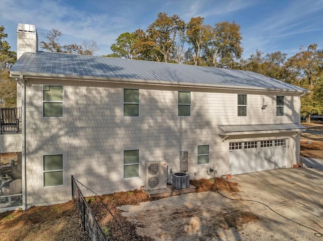 back of property with a garage, concrete driveway, a chimney, metal roof, and central AC