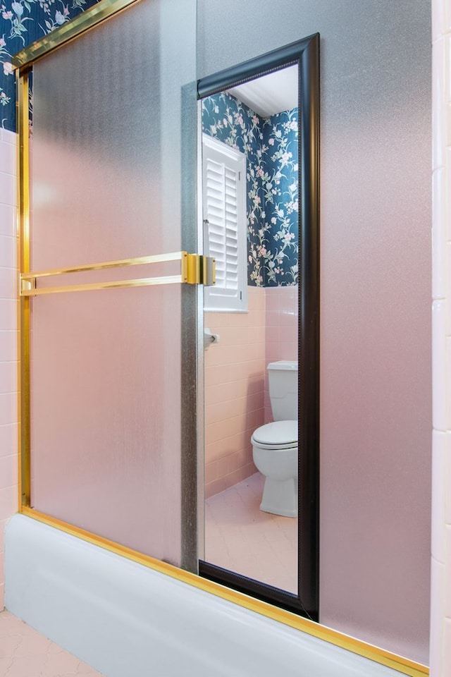 bathroom with toilet, enclosed tub / shower combo, and tile walls