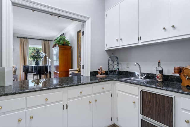 kitchen with sink, white cabinetry, dark stone counters, and crown molding